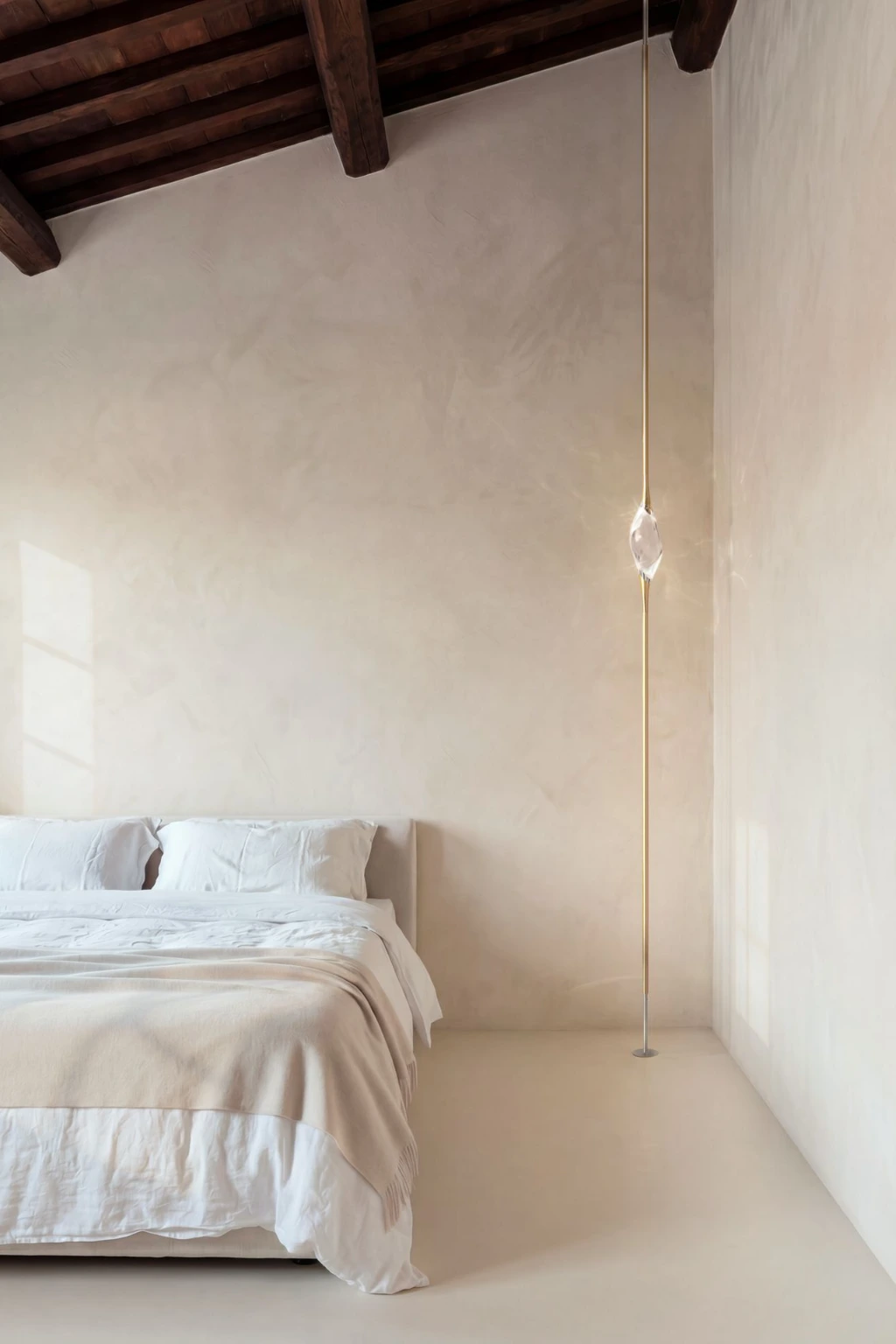Il Pezzo 12 Floor to Ceiling in satin brass finish, single solid crystal suspended on a brass rod in a white-walled bedroom with wooden ceiling beams