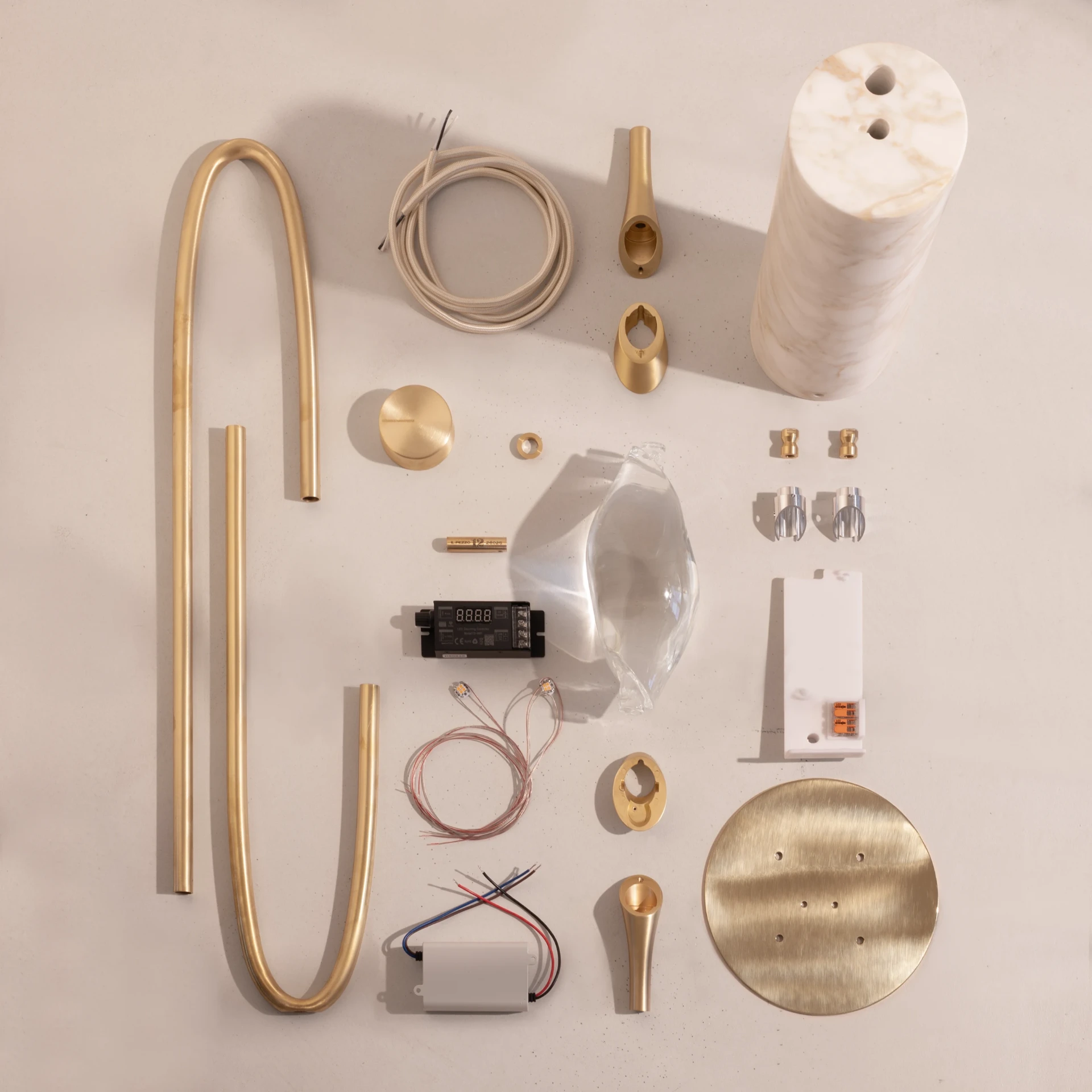 All the components of Il Pezzo 12 Floor Lamp laid out flat: brass ring, marble base, crystal, driver and Pigino